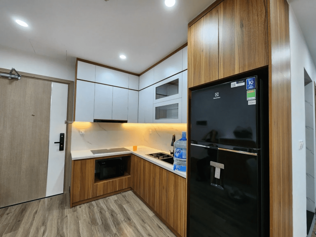 Phòng bếp căn hộ 30m2 nhỏ gọn với bố cục chữ L, tích hợp tủ lạnh, bếp từ và tủ bếp treo tiết kiệm diện tích